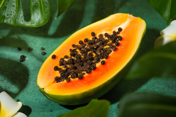 Fresh half of papaya with seeds on tropical leaves background. Tropical exotic fruit.