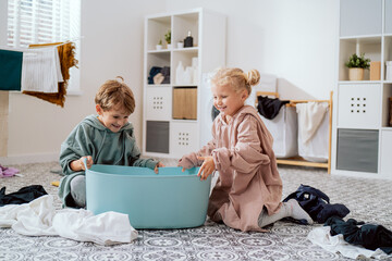 Siblings play in laundry room, bathroom with dirty clothes to be sorted, kids have thrown all the...