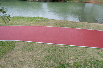 Fototapeta premium The red asphalt runway in the modern city park is surrounded by green plants on both sides