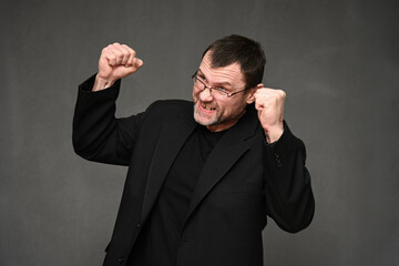 Caucasian man in a jacket with anger with fists up on a gray background