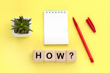 Notepad and pen on the background. Wooden cubes with word how.