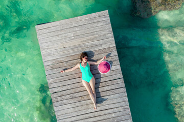Aerial view of woman laying on wooden pier at sunny summer day in Cancun, Mexico, top view. Young sexy woman wearing bright swimsuit in summertime in Caribbean. Summer beach vacation concept