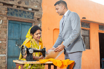 Bank person or financial advisor showing document to indian woman while she is working on sewing...