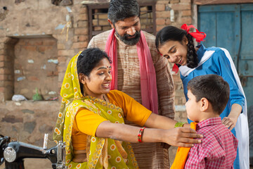 Indian mother check cloths size on her son while husband and daughter looks at him, sewing cloths on sewing machine. Small family, lifestyle.