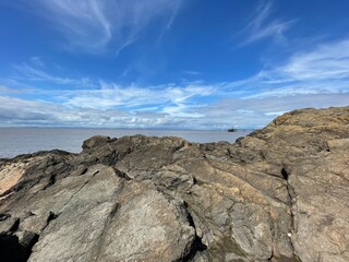 A view of the rocks at the beach leading out to the open muddy water with the beautiful blue sky in the background 