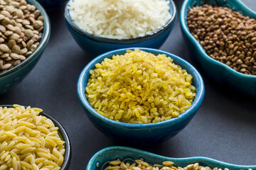 Uncooked dry cereal food group in  ceramic bowls on black surface.Selected bulgur bowl