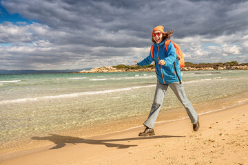Alone girl with a backpack funny jumping on the beach. The concept of hiking and activity in the...