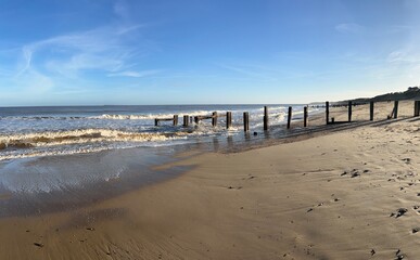 Fototapeta na wymiar Landscape of ocean from sandy beach he beautiful calm sea gentle waves and blue skies looking to horizon with wood defence structure from shore on bright cold Winter day Norfolk uk 