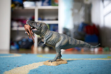 A close-up shot of a dinosaur toy holding an animal in his mouth.