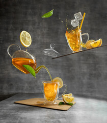levitation photo with iced tea in glass cups with lemons, fresh leafs, teapot and pouring tea over grey background. summer refreshment concept. trend balancing photo