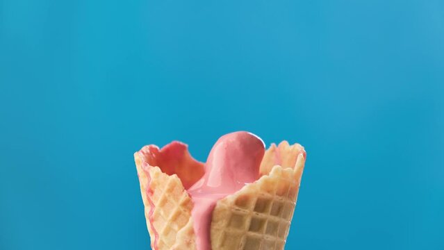 Timelapse of strawberry ice cream in waffle cone melting on blue background. Delicious pink ice cream melting. Close-up of sweet dessert. 4K, UHD