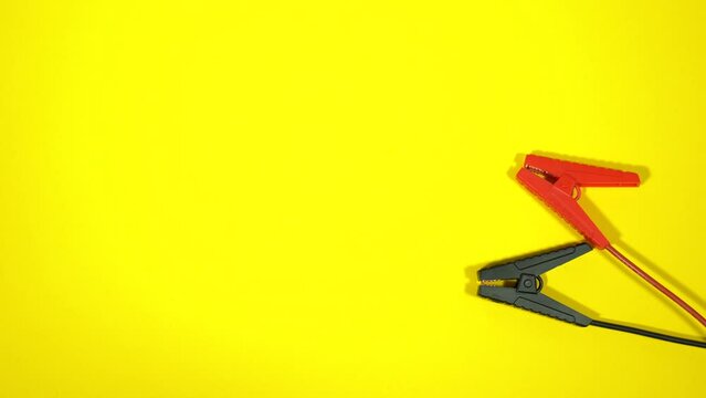 Close-up top view flatlay 4k stock video footage of male hand taking black and red vehicle jumper cables for car batteries with negative, positive clamps laying on bright yellow background