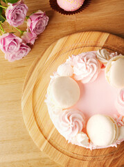 Cake for a girl. Delicate strawberry pink cake decorated with white macaroons on a wooden background. Strawberry cake on the table on March 8, Mother's Day, Valentine's Day or birthday. Space for text