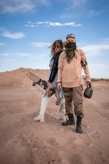 Tuinposter Couple in futuristic clothes in the desert. The woman has a bow, arrows and steampunk goggles, the man has a flask and a telescope. Post-apocalyptic cosplay of an archer and a nomad, artistic staged © evgenzz