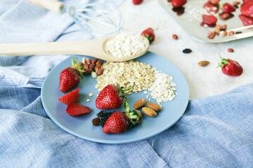 Healthy breakfast ingredients on the table, strawberries, oatmeal and nuts on a light background