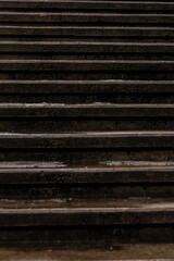 Vertical close-up photo of dark, wet, concrete set of steps at winter with ice drops. Weathered stone stairs texture for background. Pattern of dark old stairway. Wet urban lines in the city.  