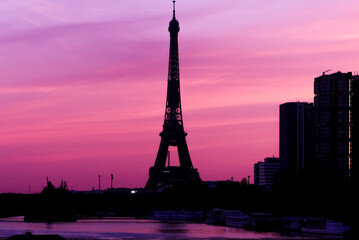 Urban landscape. View on the Eiffel tower with group of modern buildings in front of the water of Seine river. Dramatic sky with colorful clouds. Silhouette of a cityscape at sunrise.