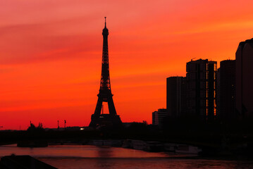 Fototapeta na wymiar Urban landscape. View on the Eiffel tower with group of modern buildings in front of the water of Seine river. Dramatic sky with colorful clouds. Silhouette of a cityscape at sunrise.