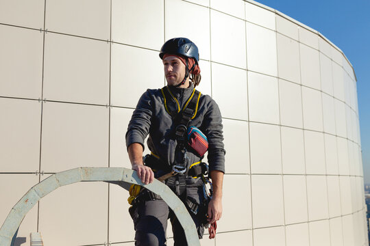 A Confident Worker In A Helmet On The Roof Of A High-rise Building. Sunny Weather, White Background