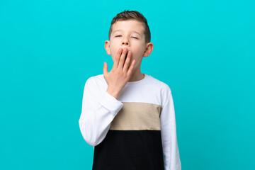 Little kid boy isolated on blue background yawning and covering wide open mouth with hand