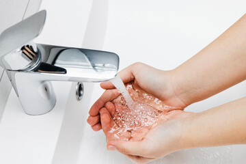 Young woman washing hands under streaming water from faucet without soap in bathroom, hygiene concept