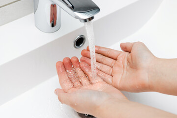 Young woman washing hands under streaming water from faucet without soap in bathroom, hygiene...