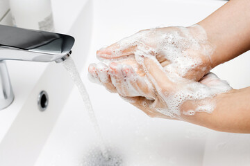 Fototapeta premium Young woman washing hands under streaming water from faucet with soap in bathroom, hygiene concept