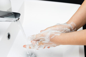 Fototapeta premium Young woman washing hands under streaming water from faucet with soap in bathroom, hygiene concept