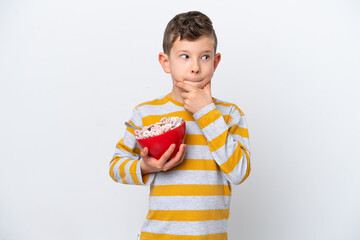 Little caucasian boy holding a cereal bowl isolated on white background having doubts and thinking