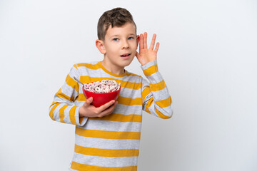 Naklejka premium Little caucasian boy holding a cereal bowl isolated on white background listening to something by putting hand on the ear