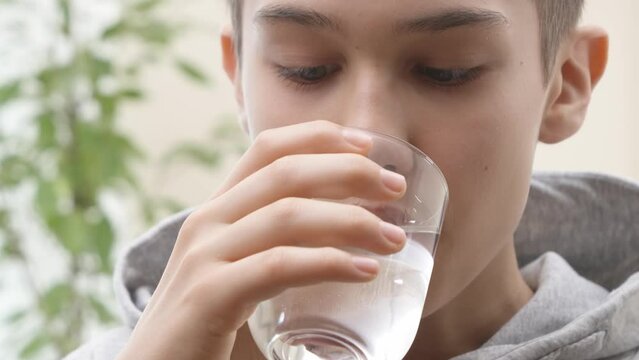 Close up of teenage boy taking vitamin D-3 softgel pill with glass of water. Healthcare and medicine concept. 4K