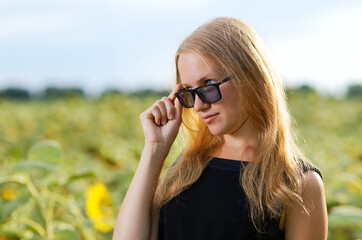 Potrait of girl with sunglasses among sunflowers field against blurred background