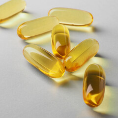 Fish oil. Yellow softgels or capsules lie on white or light gray surface. Square illustration about vitamins and healthy lifestyle. Softgel closeup. Omega-3 fatty acids. Macro