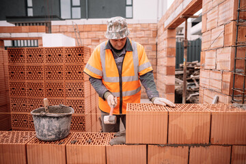 industrial bricklayer worker placing bricks on cement while building exterior walls, industry...