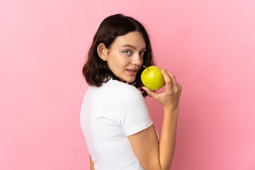 Teenager Ukrainian girl isolated on pink background eating an apple