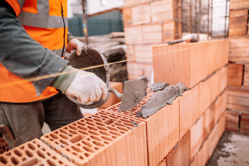 Close up details of industrial bricklayer installing bricks on industrial building, construction site - obrazy, fototapety, plakaty