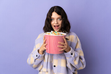 Teenager Ukrainian girl isolated on purple background holding a big bucket of popcorns