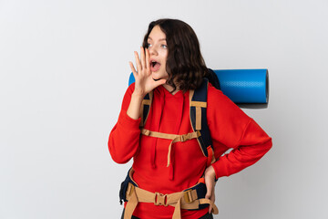 Teenager mountaineer girl with a big backpack isolated on white background shouting with mouth wide open to the side