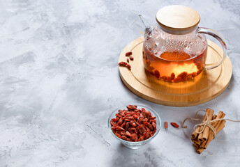 Glass teapot with hot tea with goji berries and cinnamon sticks on a bamboo stand. Selective focus.