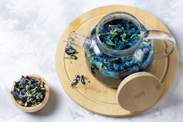 Obraz na płótnie Canvas A glass teapot made of organic blue anchana on a light table and a cup with dried tea flowers. Herbal Tea