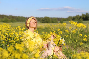 A girl with a white dog in the middle of a blooming field of yellow flowers enjoys them and...