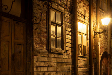 An old wooden log house with vintage doors and windows in the night illuminated by a medieval street light with copy space