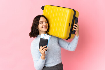 Teenager Ukrainian girl isolated on pink background in vacation with suitcase and passport