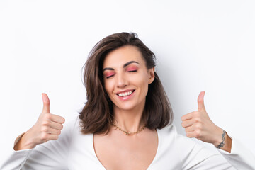 Young woman in a cocktail dress, gold chain and bright spring pink makeup on a white background. Cheerfully smiling showing thumbs up