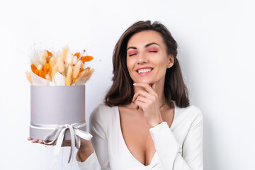 Young woman in a cocktail dress, gold chain, bright spring pink makeup on a white background. Holds a bouquet of orange dried flowers, a gift for March 8.