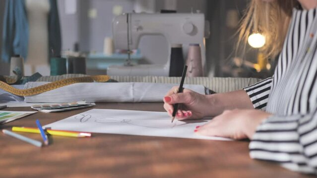 close up on female fashion designer hand drawing clothes sketches,woman stylist at her workplace creating designs fashionable garments collection in studio