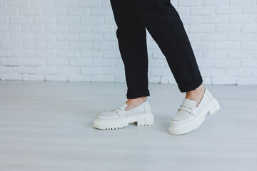 Legs of a young beautiful woman in black trousers and modern stylish white leather loafers. New...