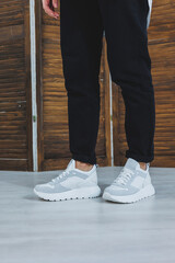 Beautiful women's shoes with legs, leather white sneakers, in the interior of a room or office, shoes for a woman, black trousers and white sneakers, casual and modern style, modern and trendy