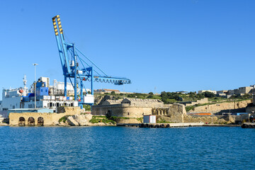Fototapeta na wymiar Paola, Malta - Remains of the Corradino Lines fortifications built in the 1870’s and the Ras Ħanżir Polverista (gunpowder store) built in 1756. In the background are cranes at the Paola dockyards.