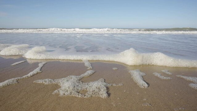 POV of gentle foamy waves moving up towards a pristine beach on the North Sea, Belgian coast